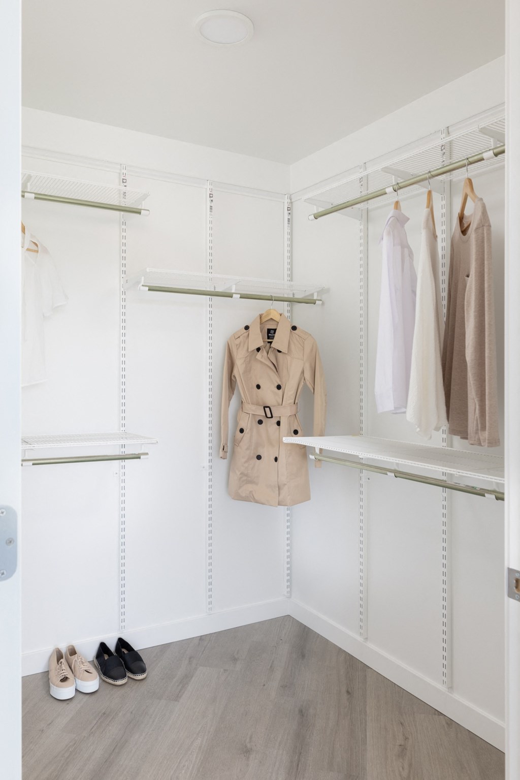a walk in closet with white walls and shelves and a coat rack
