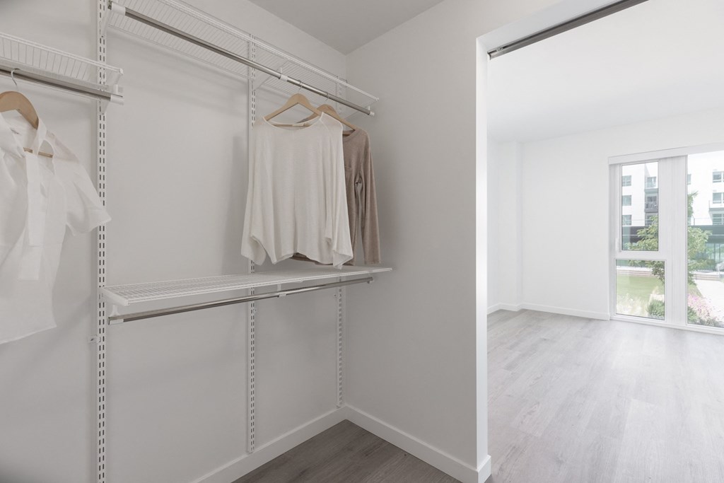 a walk in closet with a mirrored closet door and two white dresses on hanging racks