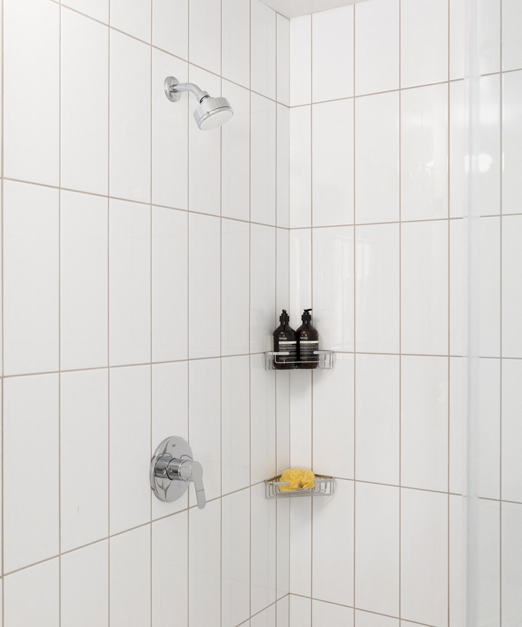 a white tiled bathroom with a shower and two bottles in it