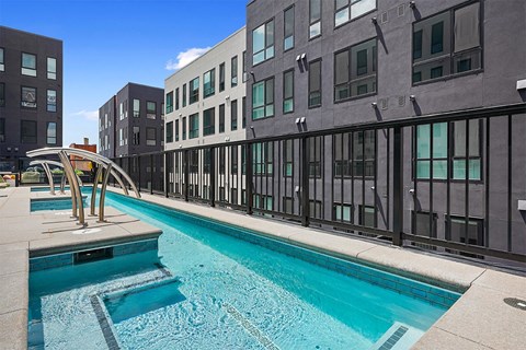 A swimming pool is surrounded by a black fence and a building.