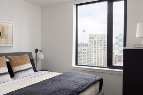 A bedroom with a large bed and a window overlooking a cityscape.
