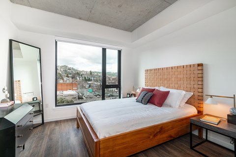 A bedroom with a large bed, a desk, and a view of the city through the window.