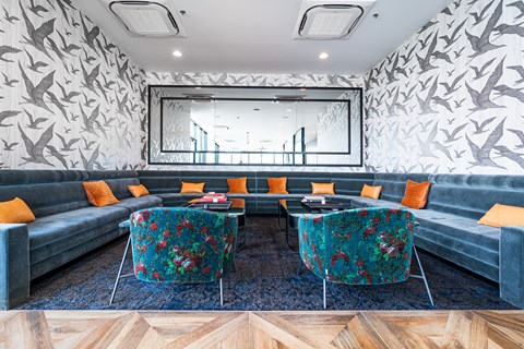 A grey couch with orange pillows is in front of a grey wall with a bird pattern.