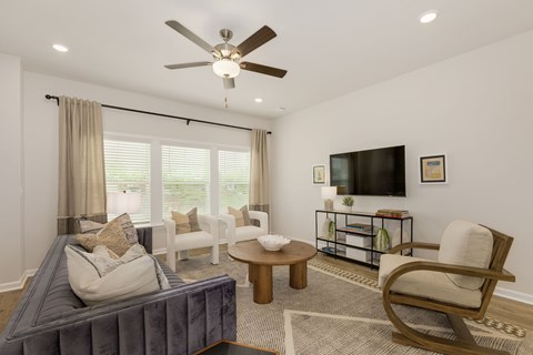 A living room with a grey couch, a wooden coffee table, a television, and a ceiling fan.