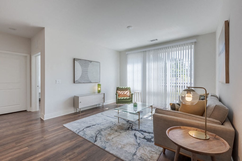 Newry Mill living room. Photo includes floor-to-ceiling windows along with chairs, a couch, coffee tables, blinds, and a rug (furniture not included).