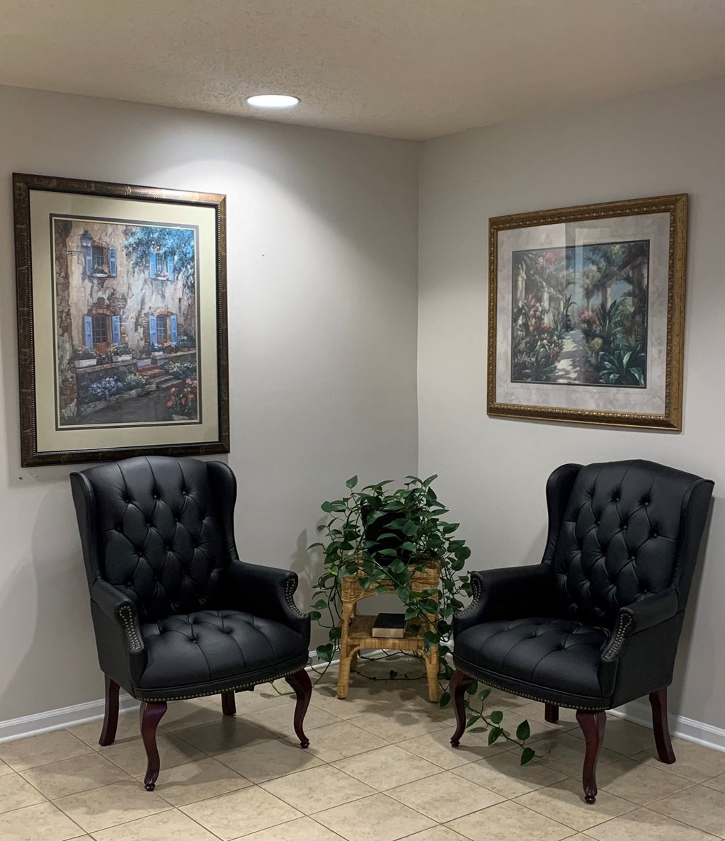 Two black chairs are placed in front of two framed pictures.