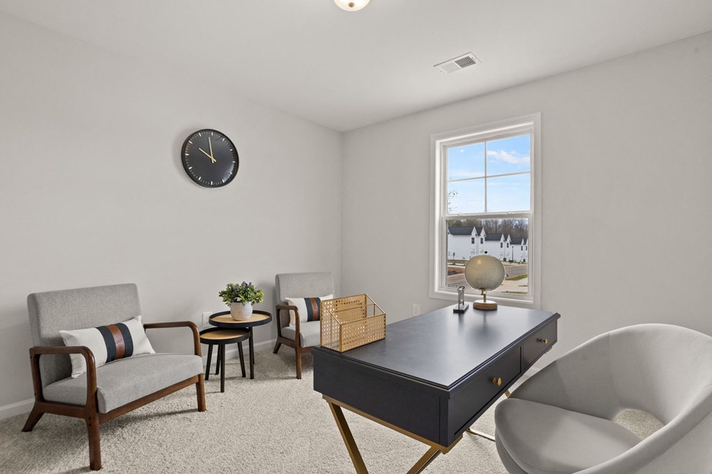 a living room with a desk and chairs and a window