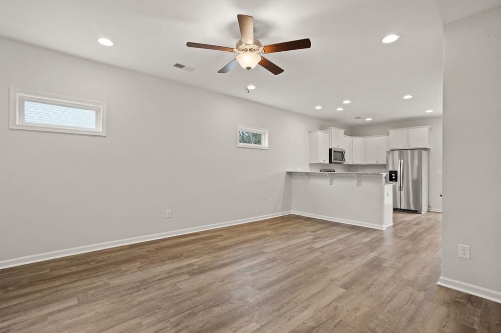 an empty living room with a ceiling fan and a kitchen
