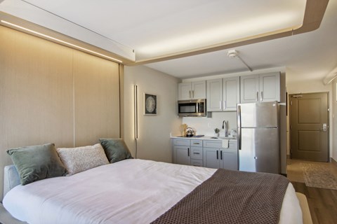 a bedroom with a bed and a kitchen with a refrigerator