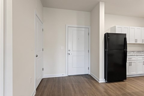A black refrigerator stands in a kitchen with white cabinets.