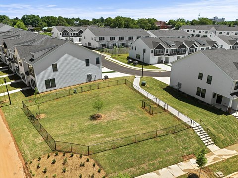 A large grassy area surrounded by a fence with a few trees and houses in the background.