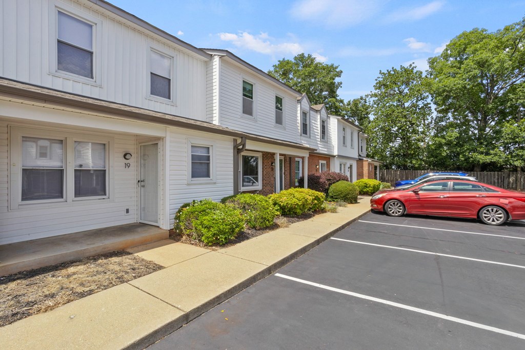 A red car is parked in a parking lot in front of a white building.