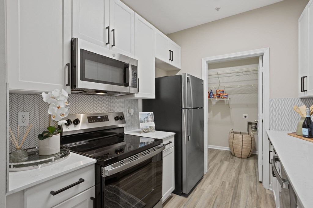 Flatiron West Trade Apartments staged model unit kitchen connected to living room with stainless steel modern appliances and quartz countertops