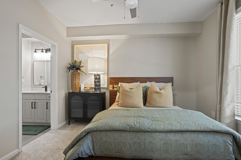 Flatiron West Trade Apartments staged model unit bedroom with gray carpet, attached bathroom with walk-in closet, and a ceiling fan