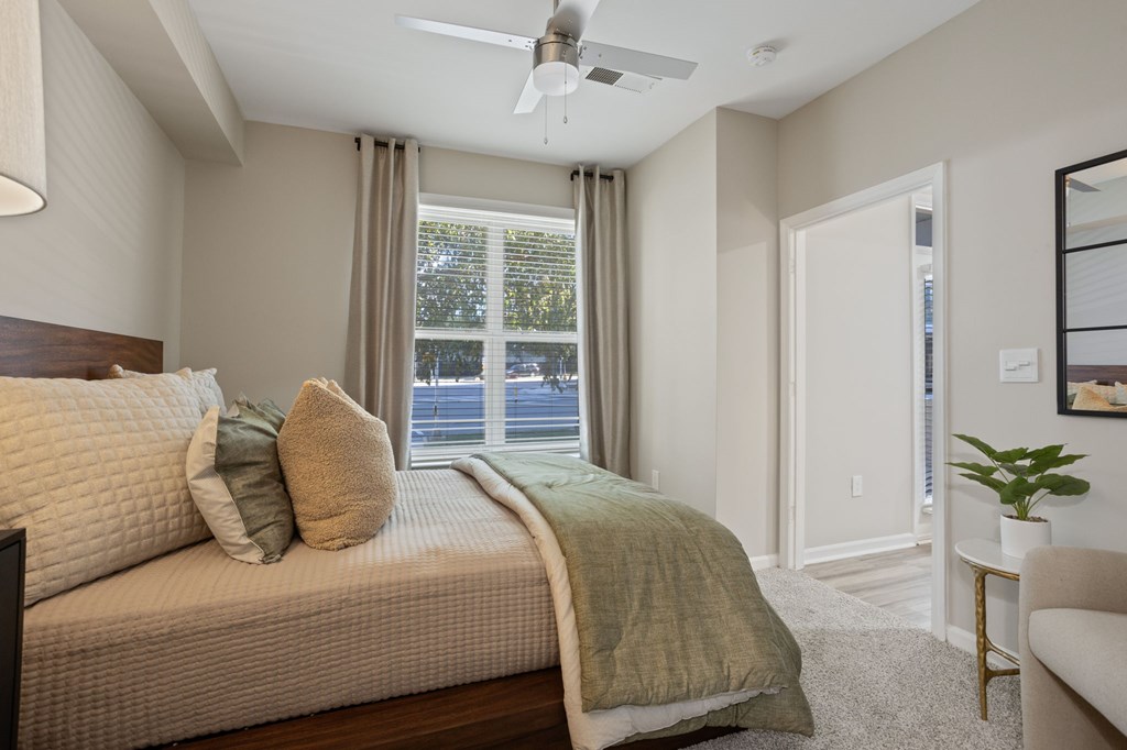 Flatiron West Trade Apartments staged model unit bedroom with gray carpet, attached bathroom with walk-in closet, and a ceiling fan