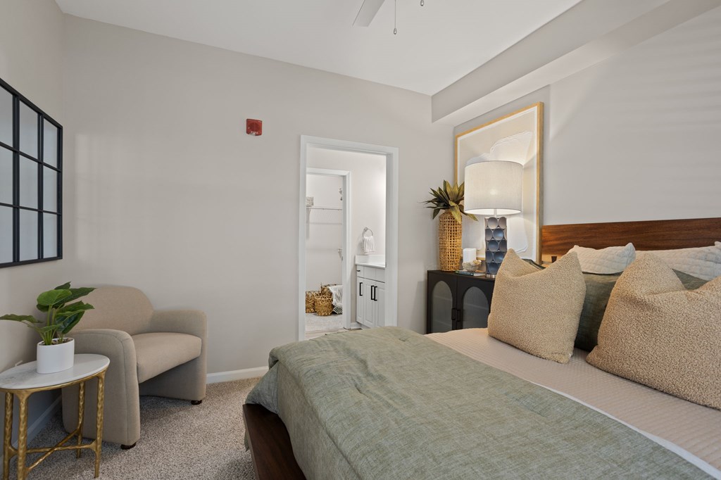 Flatiron West Trade Apartments staged model unit bedroom with gray carpet, attached bathroom with walk-in closet, and a ceiling fan