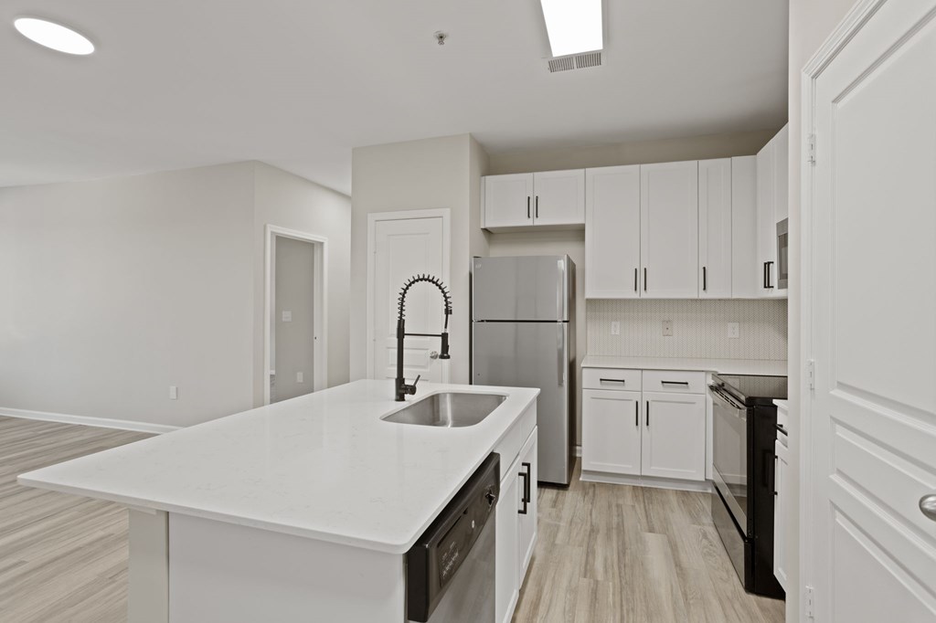 Flatiron West Trade Apartments staged model unit kitchen connected to living room with stainless steel modern appliances and quartz countertops