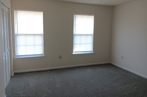 an empty room with two windows and a carpet