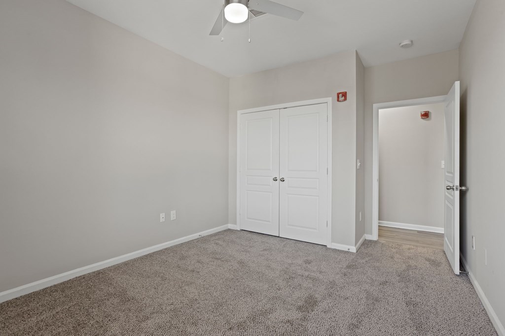 A room with a carpeted floor, a closet and a ceiling fan.