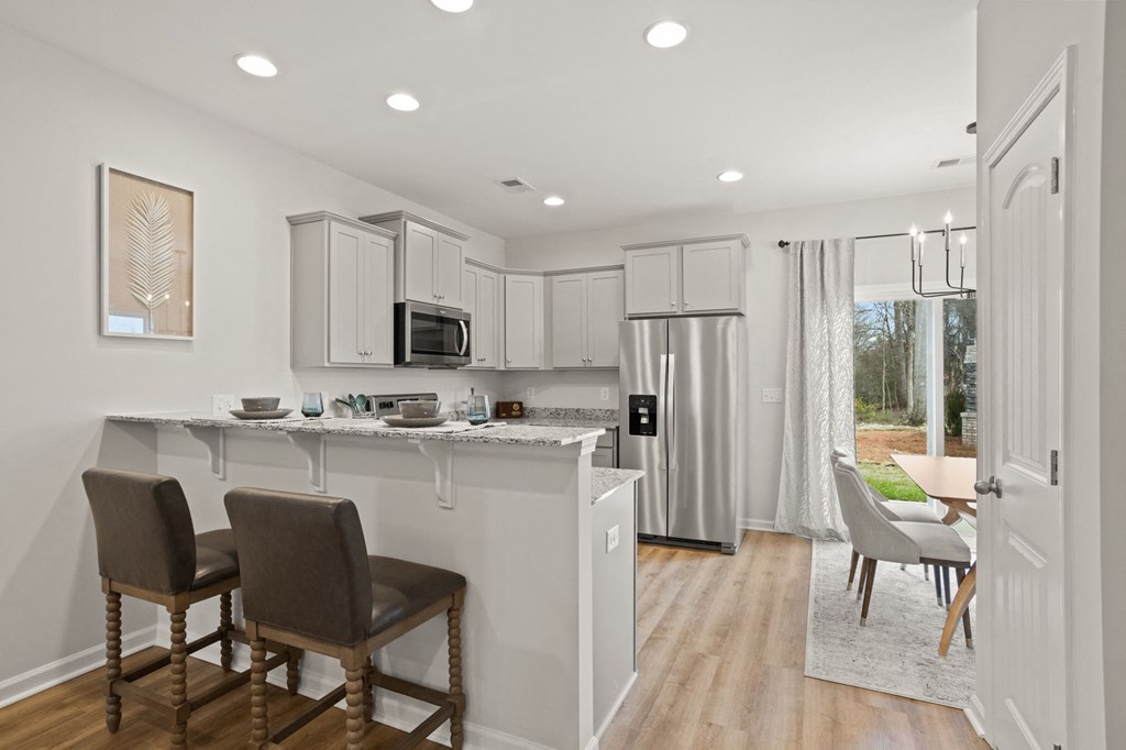 a kitchen with white cabinets and a bar with two chairs