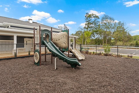 A playground with a green slide and brown ground.