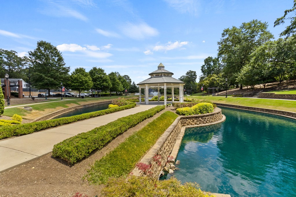A gazebo is situated in the middle of a garden with a pond.