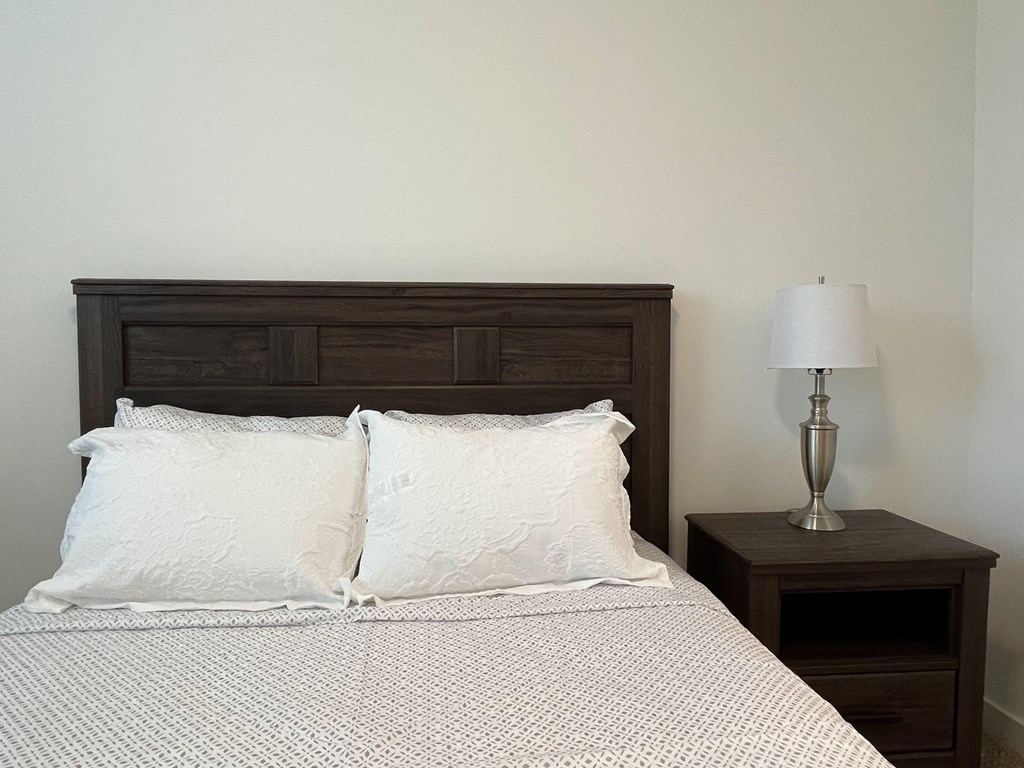A bedroom with a bed and a nightstand with a lamp in The Alston Apartments.