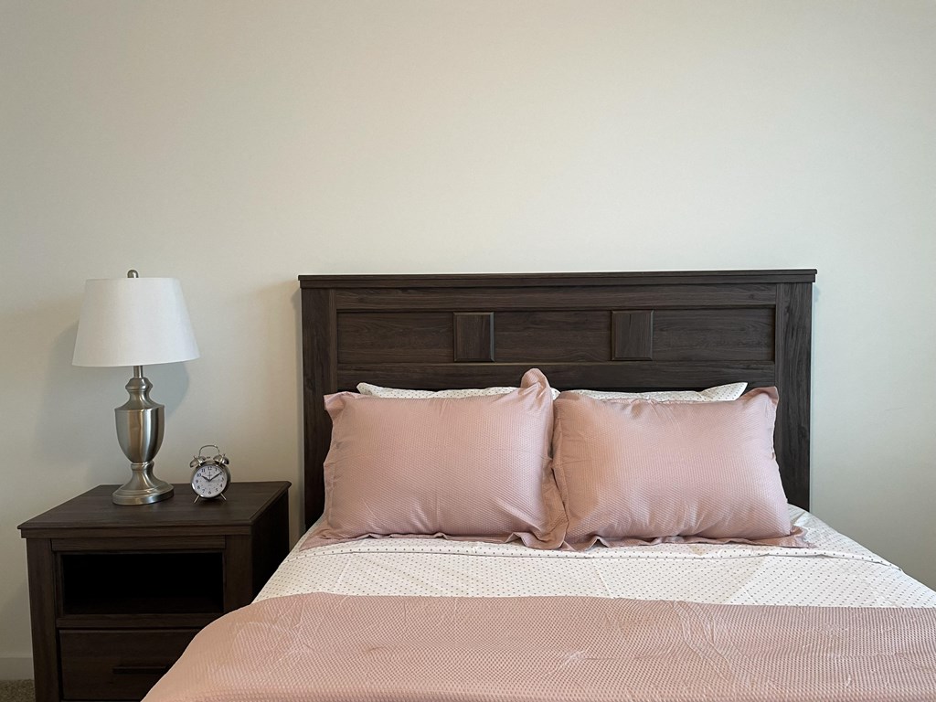 A bedroom with a bed with pink pillows and a wooden headboard in The Alston Apartments.