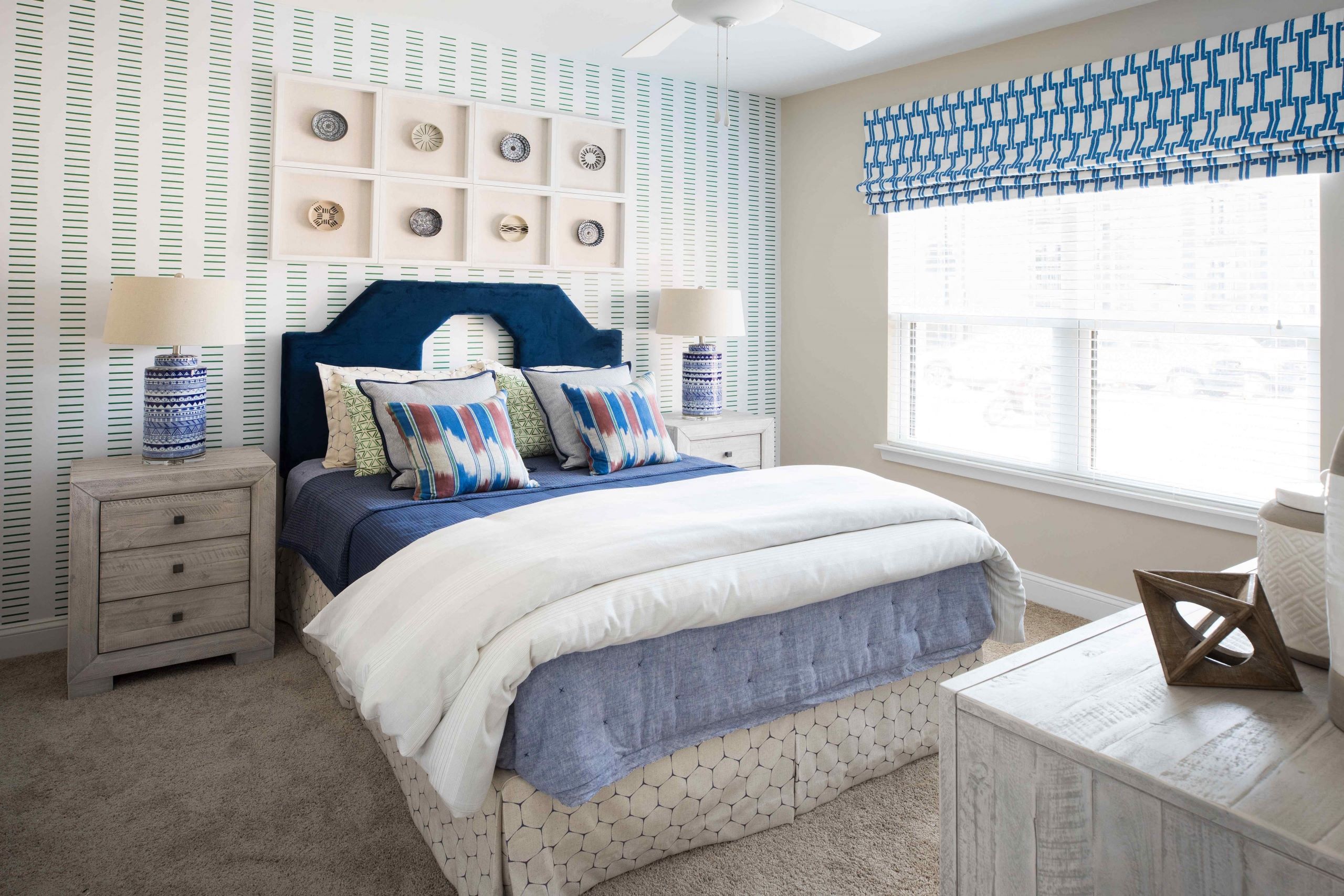 A bedroom with a bed, nightstands, and a window with a blue and white striped valance.