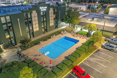 A swimming pool is surrounded by a hedge and a red van is parked in the parking lot.