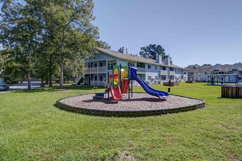 A playground with a red slide and a blue slide in front of a white building.