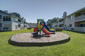 A playground with a red slide and a green slide in the middle of a grassy area.
