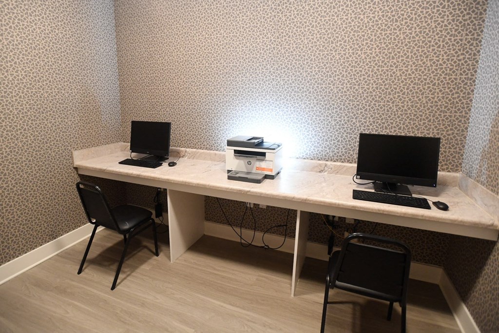A white desk with two laptops and a stack of books under a lamp.