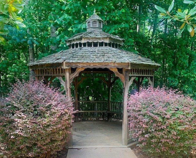 A gazebo surrounded by green trees and pink flowers.