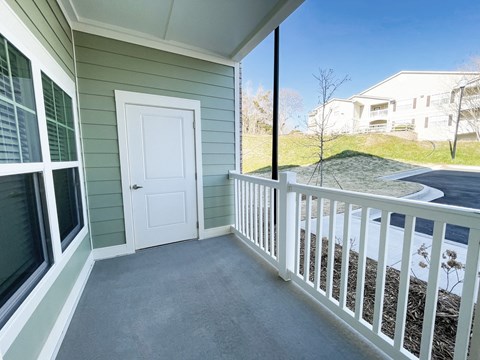 A white door is on the left side of a porch with a white railing.
