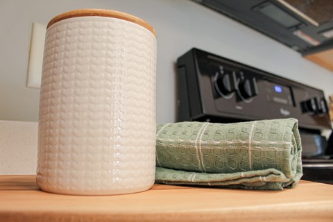 A white textured container sits on a counter next to a green towel.