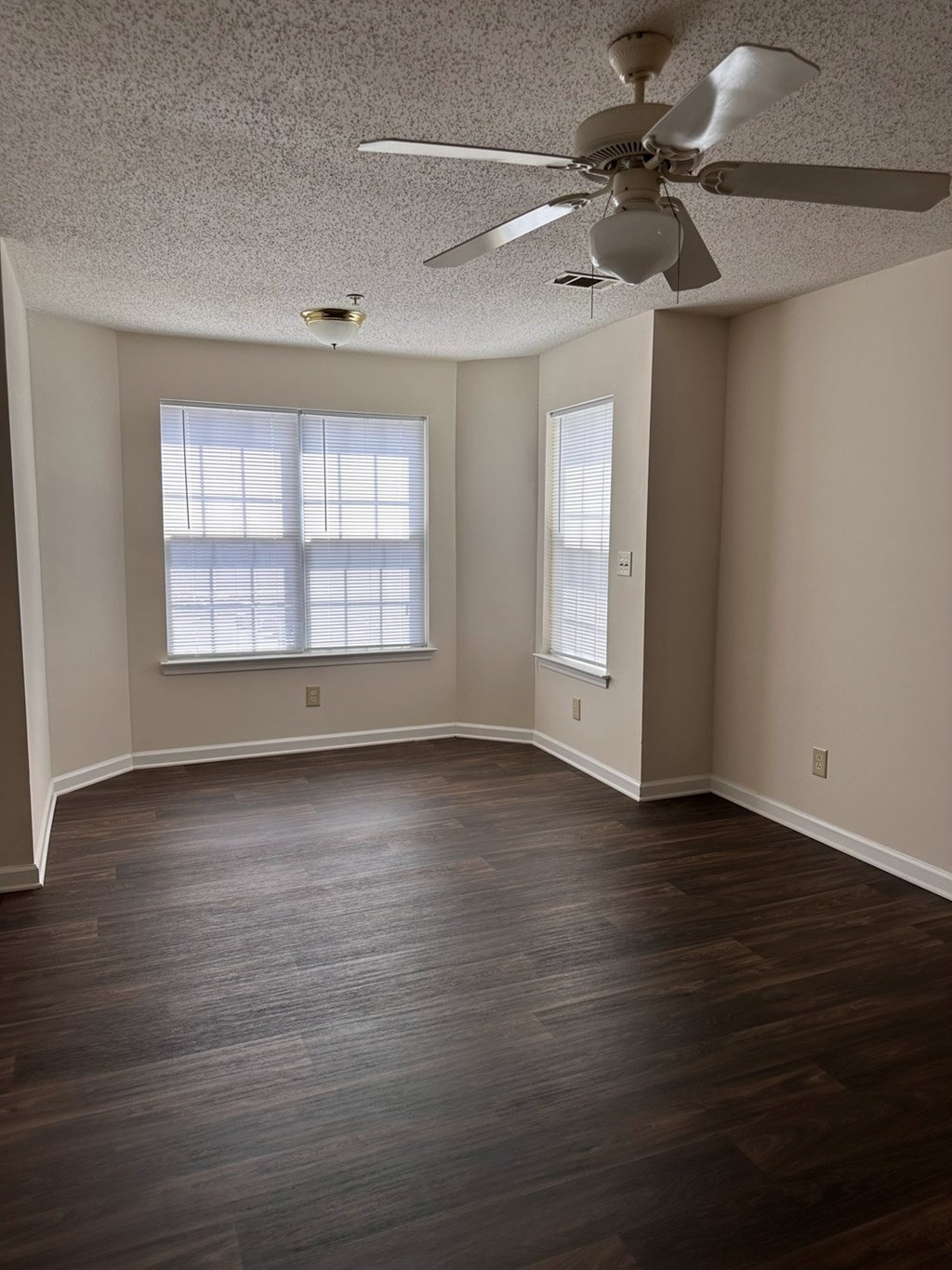 A room with a ceiling fan and two windows.