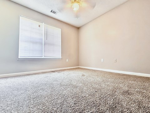 A room with a carpeted floor and a window with blinds.