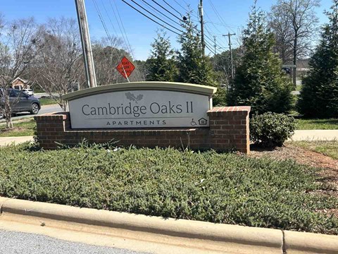 A sign for Cambridge Oaks II Apartments is displayed in front of a hedge.