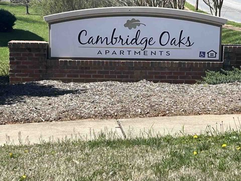 A sign for Cambridge Oaks Apartments is displayed in front of a grassy area.