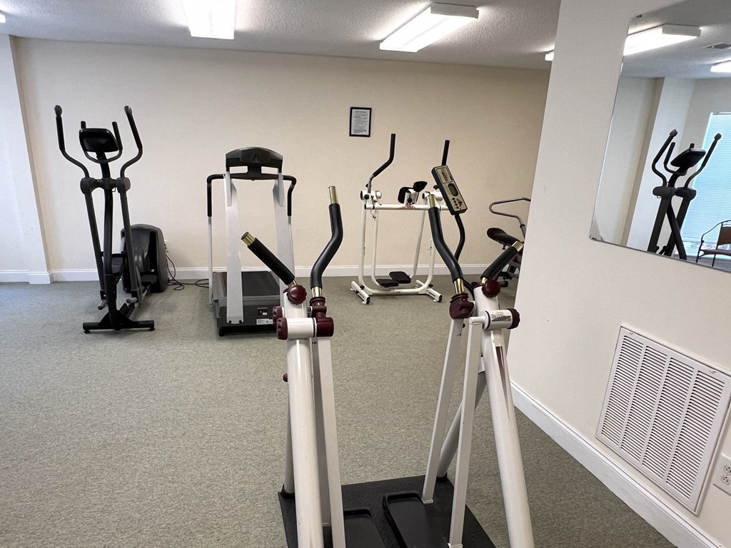A gym with exercise equipment and mirrors on the wall.