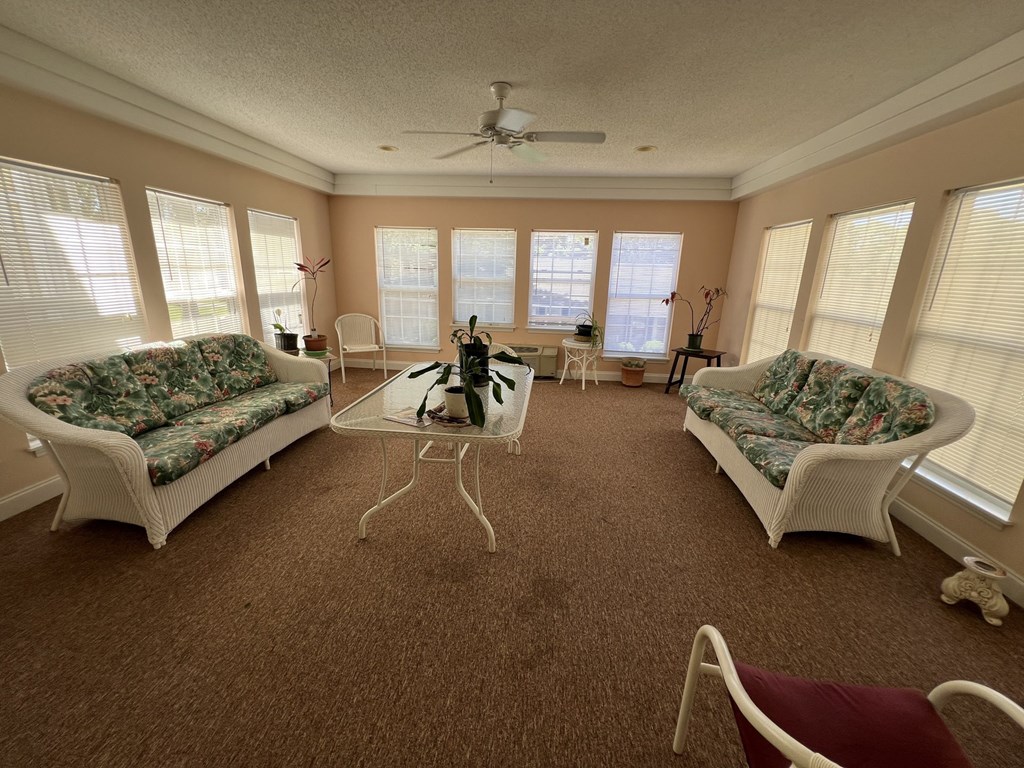 A sunny day in a living room with a fan, two couches, a coffee table, and a dining table.