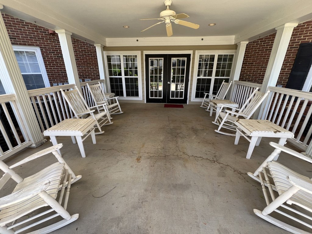 A porch with white chairs and a ceiling fan.