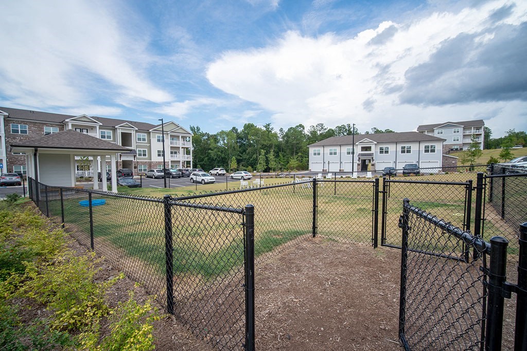 a fenced in dog park in front of apartment buildings