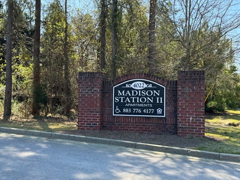 A sign for Madison Station II Apartments stands in front of a wooded area.