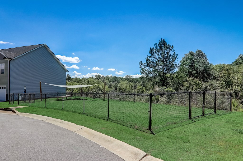 Dog-Friendly Townhomes In Greenville, SC - Marbella Townhomes - A Dog Park With Green Grass, Secure Fencing, Shaded Areas, Clear Signage, And Surrounded By Trees.