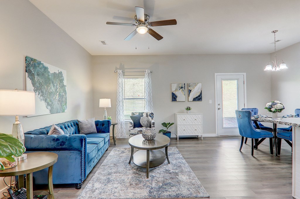 Pet-Friendly Townhomes In Greenville, SC - Marbella Townhomes - A Living Area With A Blue Velvet Sofa, Modern Decor, Hardwood Flooring, Elegant Lighting, And A Ceiling Fan.