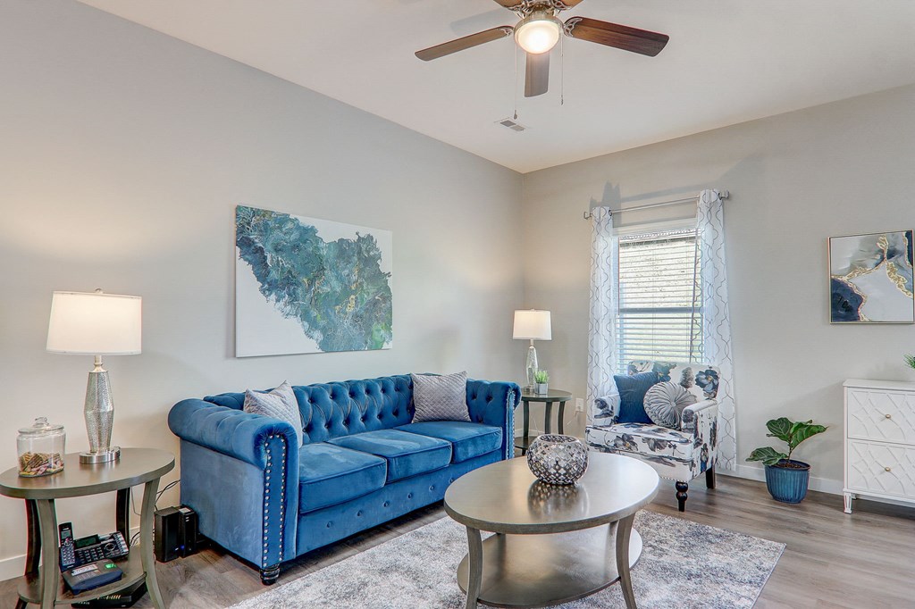 Pet-Friendly Townhomes In Greenville, SC - Marbella Townhomes - A Living Area With A Blue Velvet Sofa, Modern Decor, Hardwood Flooring, Elegant Lighting, And A Ceiling Fan.