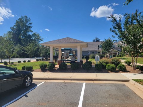A black car is parked in a parking lot in front of a building with a covered walkway.