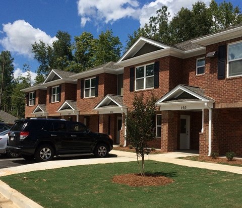 A black SUV is parked in front of a brick house with the number 150 on the front door.